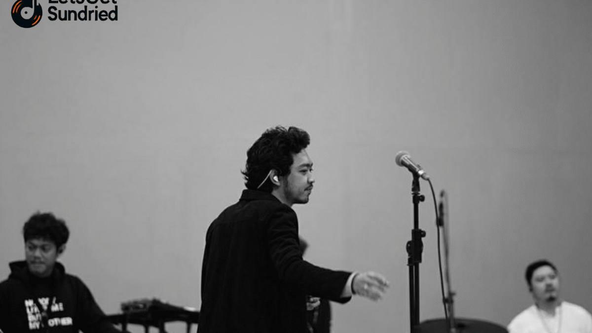 Foto hitam putih Pamungkas sedang menyanyikan lagu 'To The Bone' di atas panggung dengan pencahayaan dramatis, merepresentasikan inti dari kisah di balik MV.