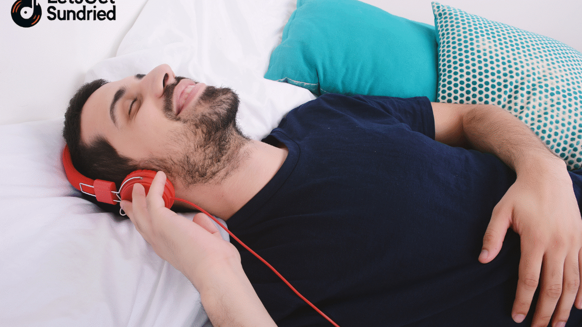 Pria sedang mendengarkan musik dengan earphone sambil tidur nyenyak, menunjukkan efek menenangkan dari playlist tidur nyenyak.