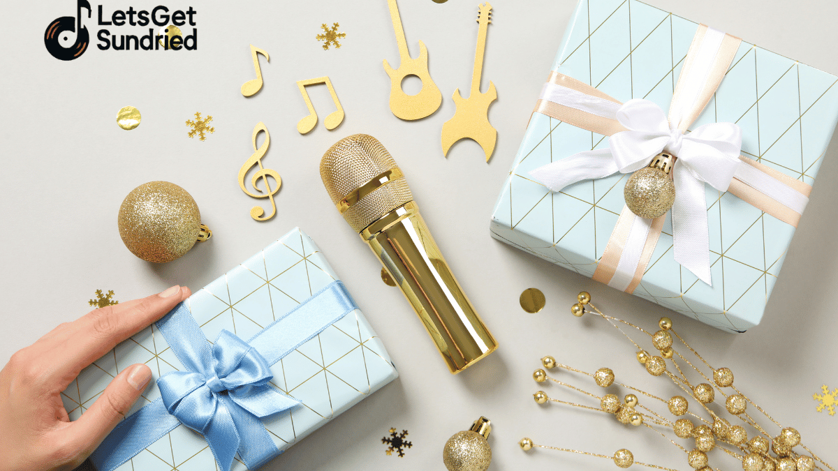 Flat lay mikrofon emas, dua kotak kado biru, dan konfeti not musik di atas meja putih