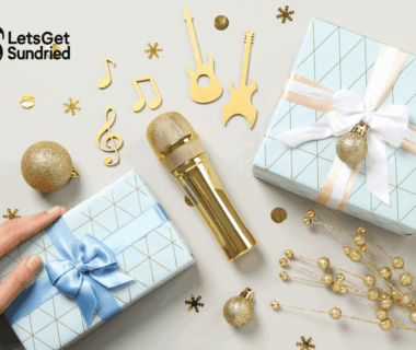 Flat lay mikrofon emas, dua kotak kado biru, dan konfeti not musik di atas meja putih