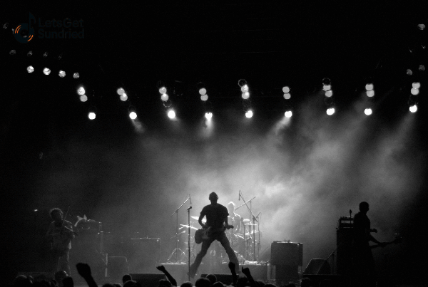 "Siluet band rock tampil di panggung dengan pencahayaan dramatis, menggambarkan sejarah musik rock dan energinya."