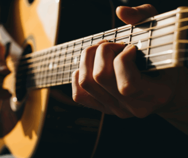 Jari tangan menekan chord gitar akustik dengan cahaya matahari masuk